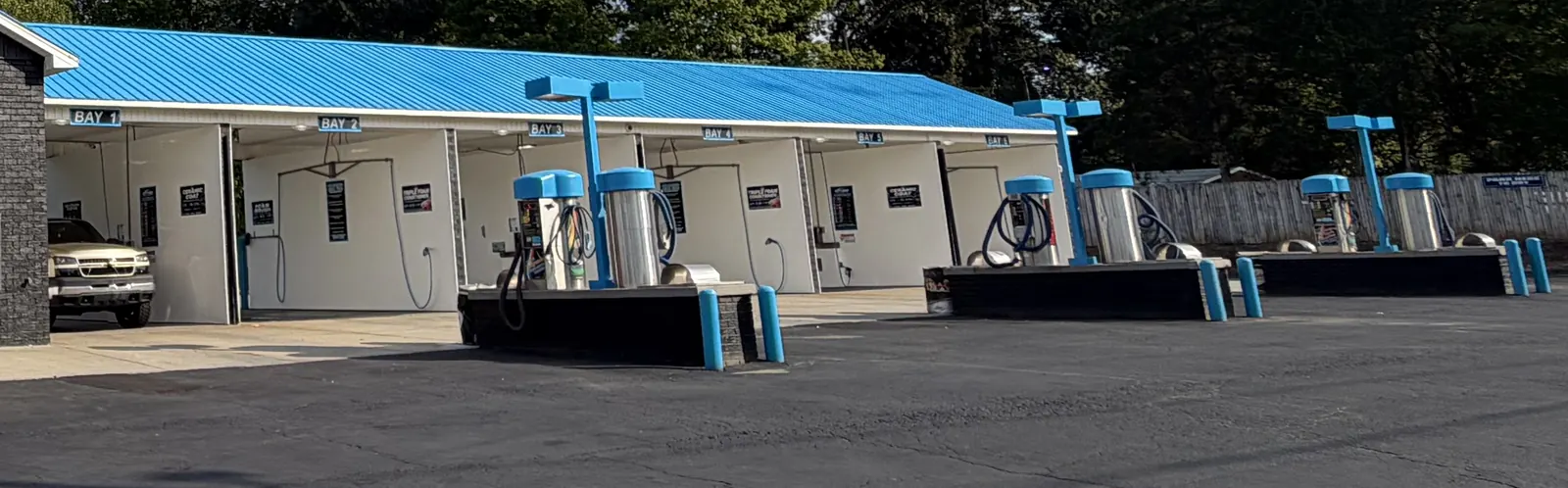 Row of self-serve wash bays with blue pressure wands and pay boxes